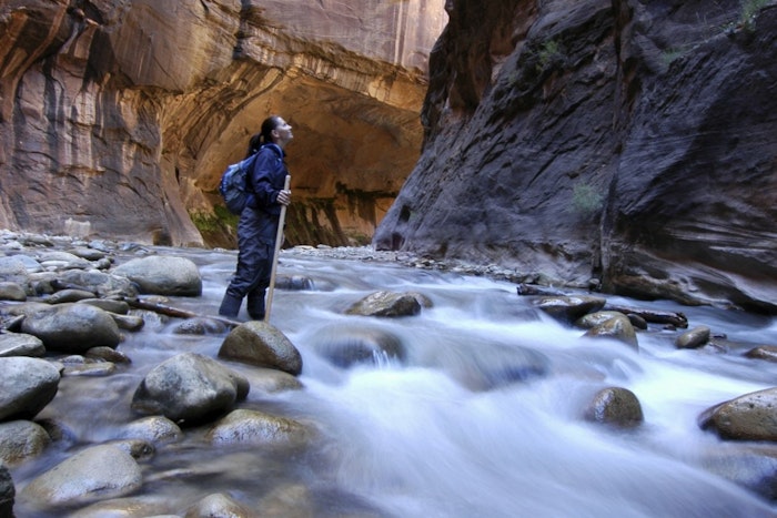A person stands at the bottom of a canyon as a stream glides across smooth-faced rocks on the ground