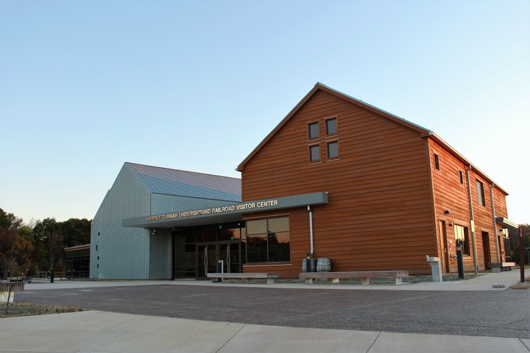 Front view of the visitor center, with two barn-like fronts visible, one in orange wood panel and one in metallic gray
