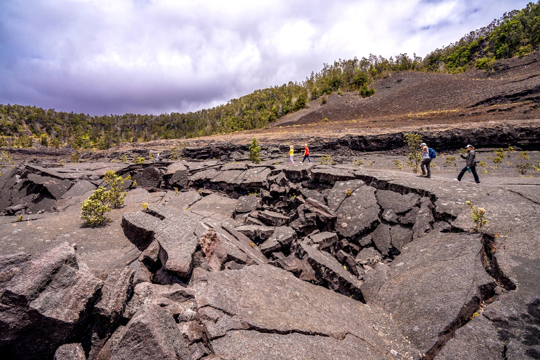 Hikers walk across rough, hardened lava on a crater floor