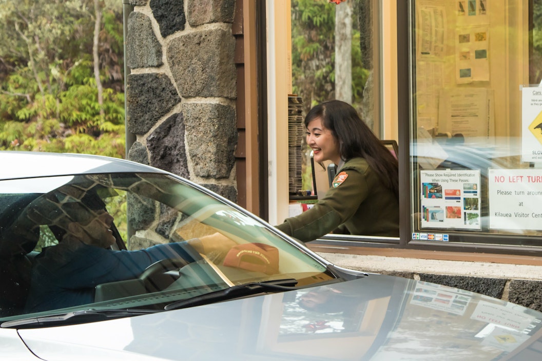 A park ranger, in uniform, reaches out to a visitor in a car