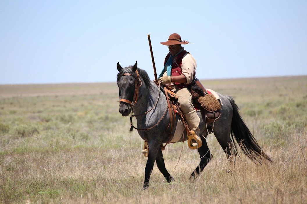 A person wearing period costume rides a black horse through the plains