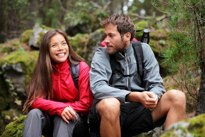 Two people dressed in hiking gear sit next to each other and smile