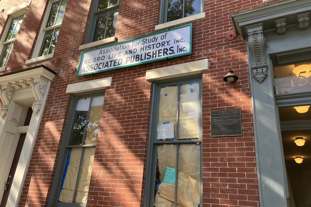 A recreation of a historic sign, hung outside a red brick building, reads "Association for the Study of Negro Life and History, Inc. Associated Publishers, Inc."