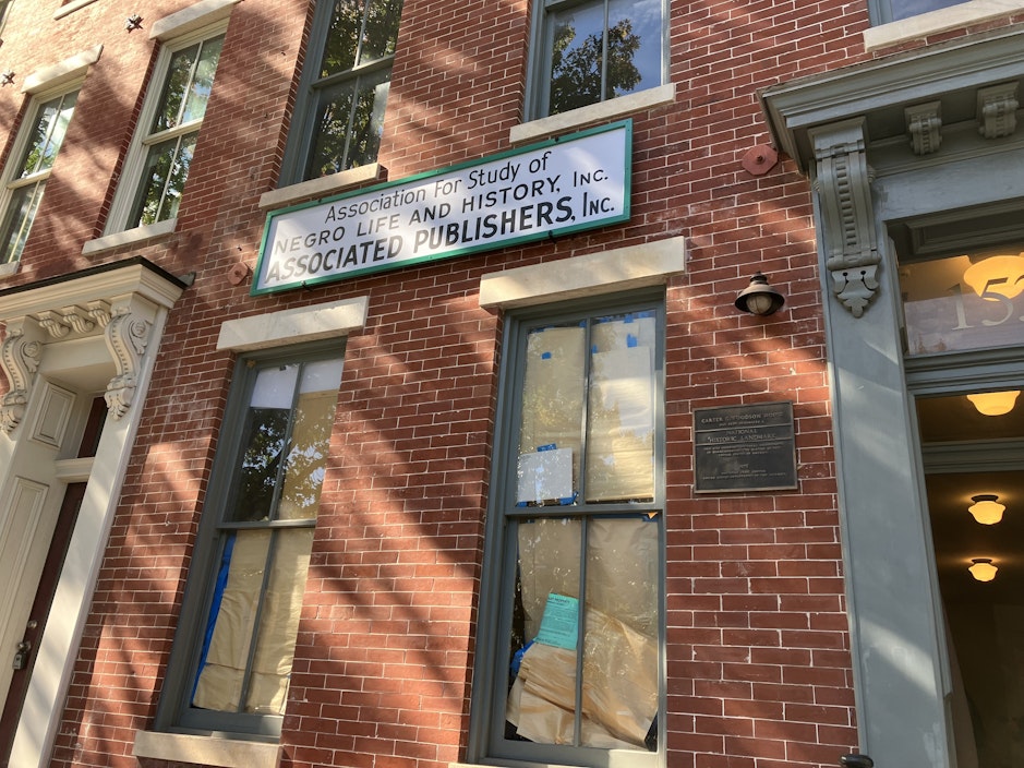 A recreation of a historic sign, hung outside a red brick building, reads "Association for the Study of Negro Life and History, Inc. Associated Publishers, Inc."