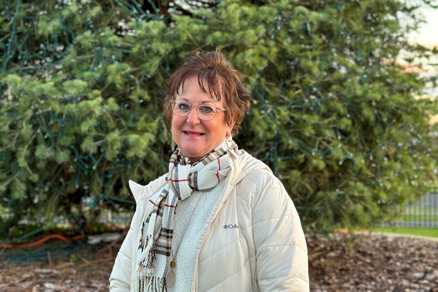 Debbie George stands in front of an evergreen tree