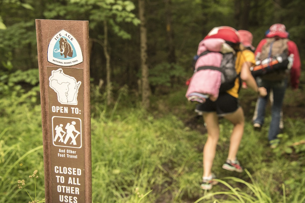 Hikers with large packs walk past a trail marker for the Ice Age National Scenic Trail