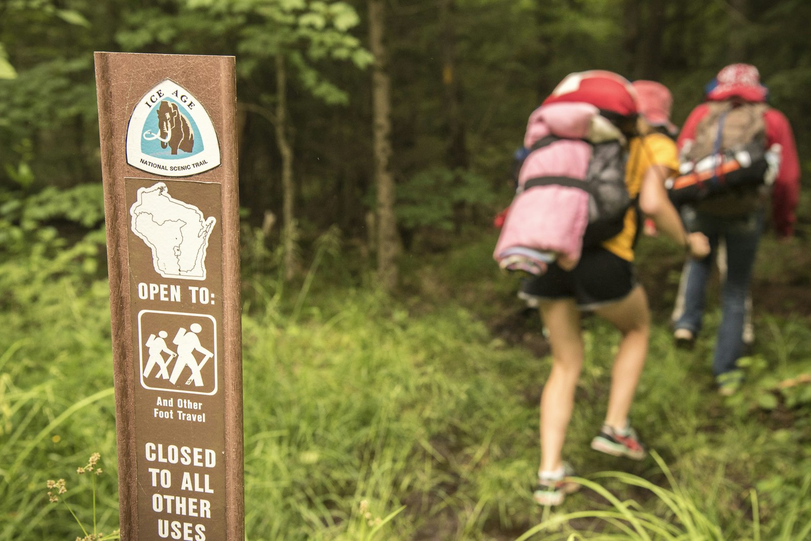 Hikers with large packs walk past a trail marker for the Ice Age National Scenic Trail