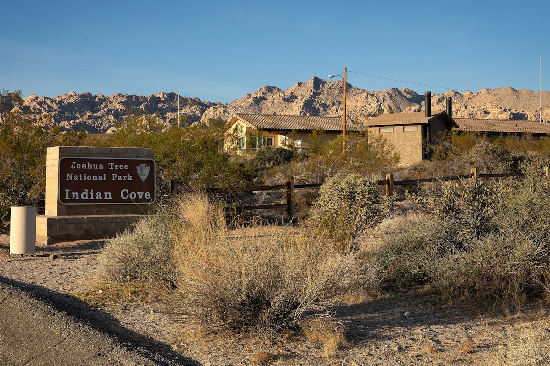A sign that reads, Joshua Tree National Park, Indian Cove, with a building in the background.