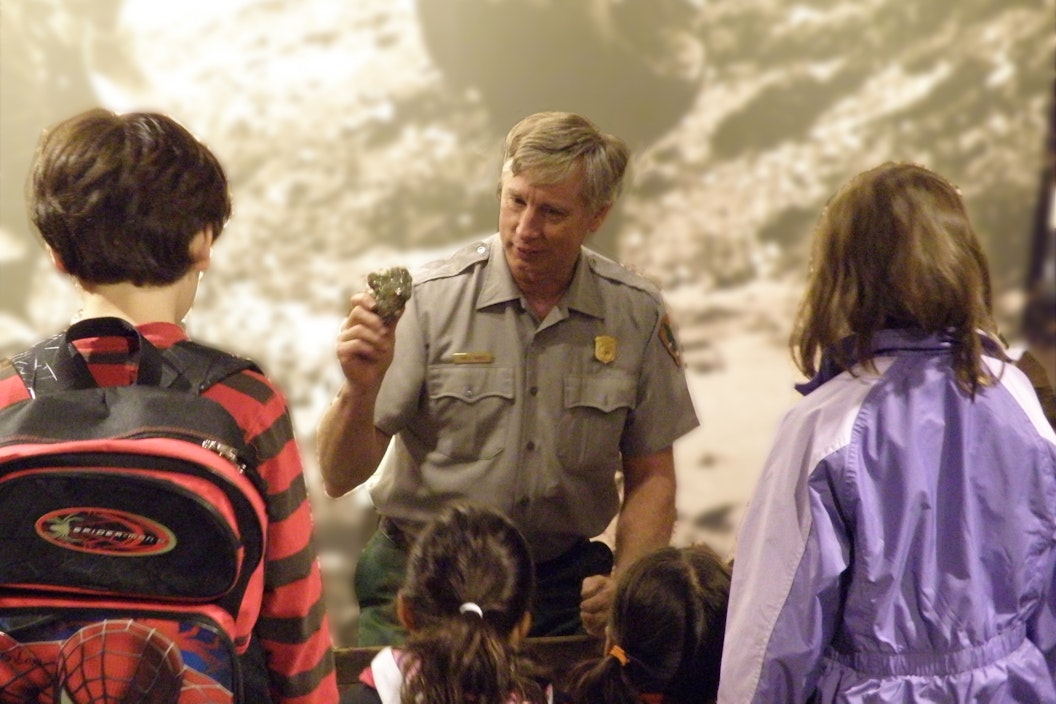 A ranger holds up a piece of rock, with small glints of gold, in front of a group of students