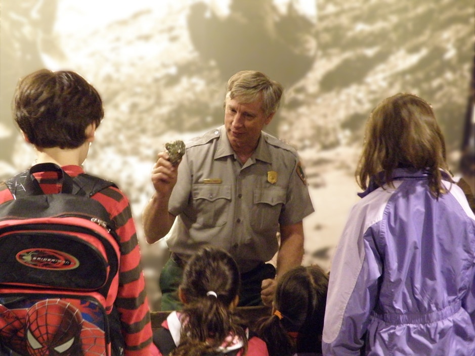 A ranger holds up a piece of rock, with small glints of gold, in front of a group of students