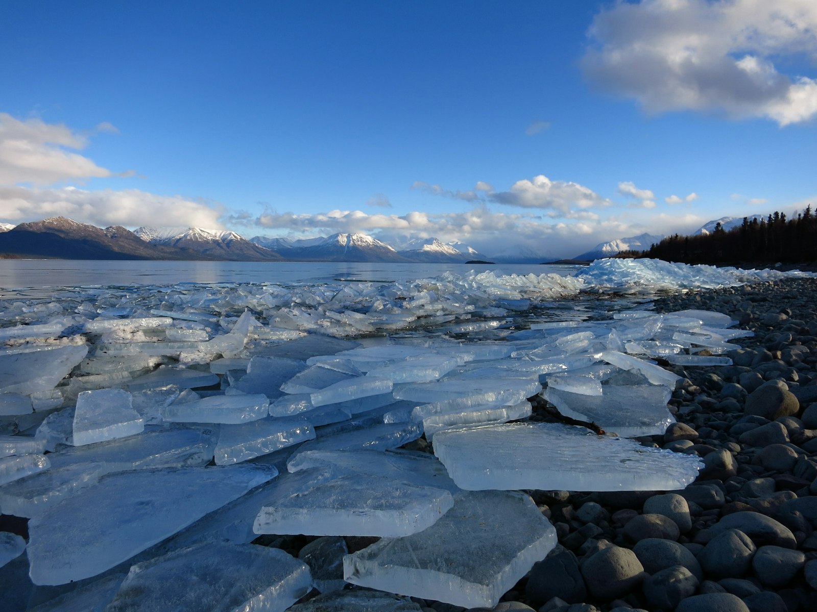 Blocks of ice atop a rocky beach. In the distance you can spot snow-topped mountain ranges