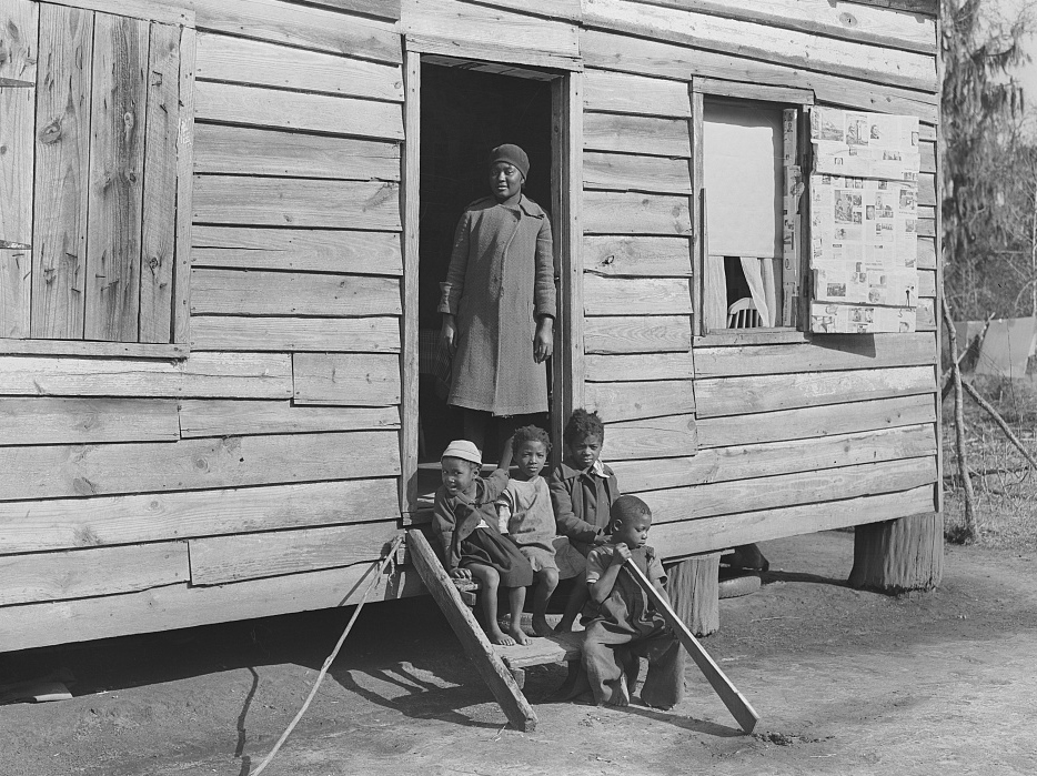 Historic photo of a family sitting and standing outside a wooden building
