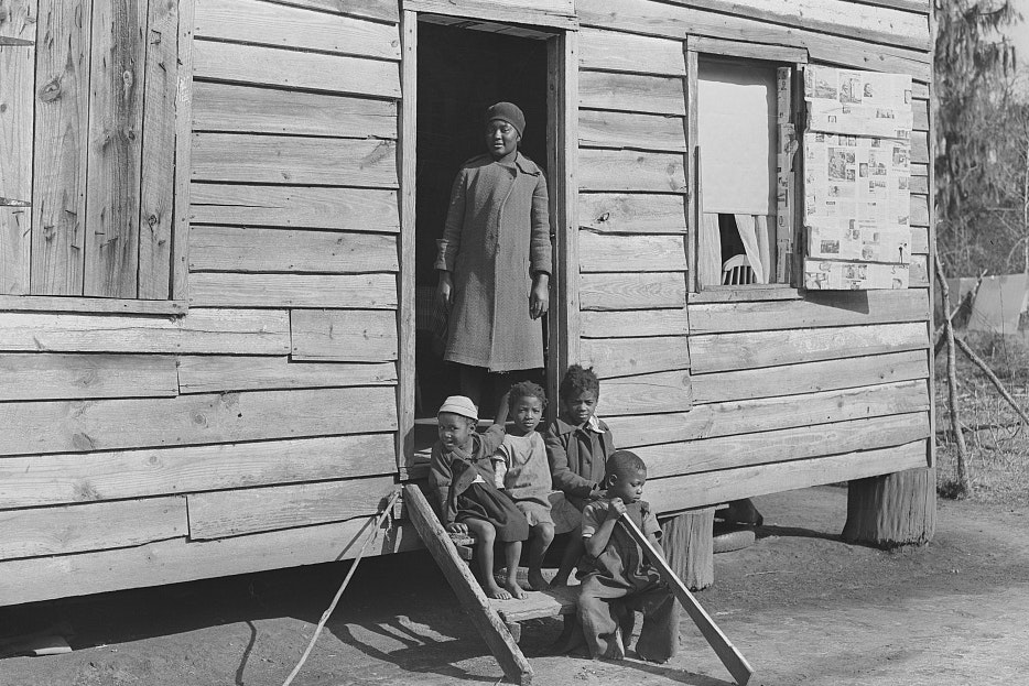 Historic photo of a family sitting and standing outside a wooden building