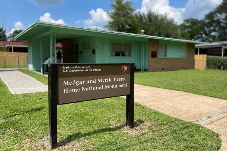 Sign in front of a one-story teal home with a carport. The sign reads: Medgar & Myrlie Evers Home National Monument