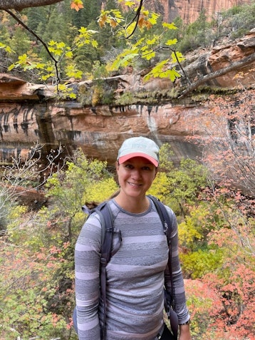 A woman wearing a backpack and cap posing for a photo at Zion National Park