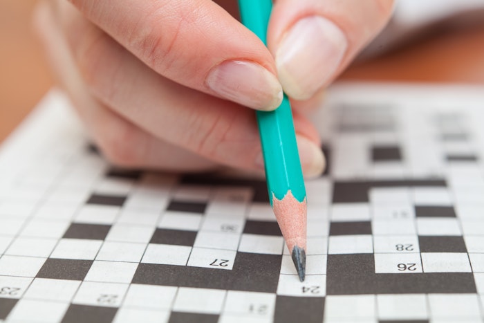 A close-up image of a teal pencil filling in a crossword puzzle