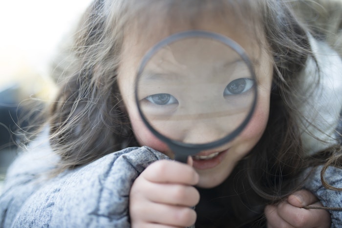 A small child looks through a large magnifying glass