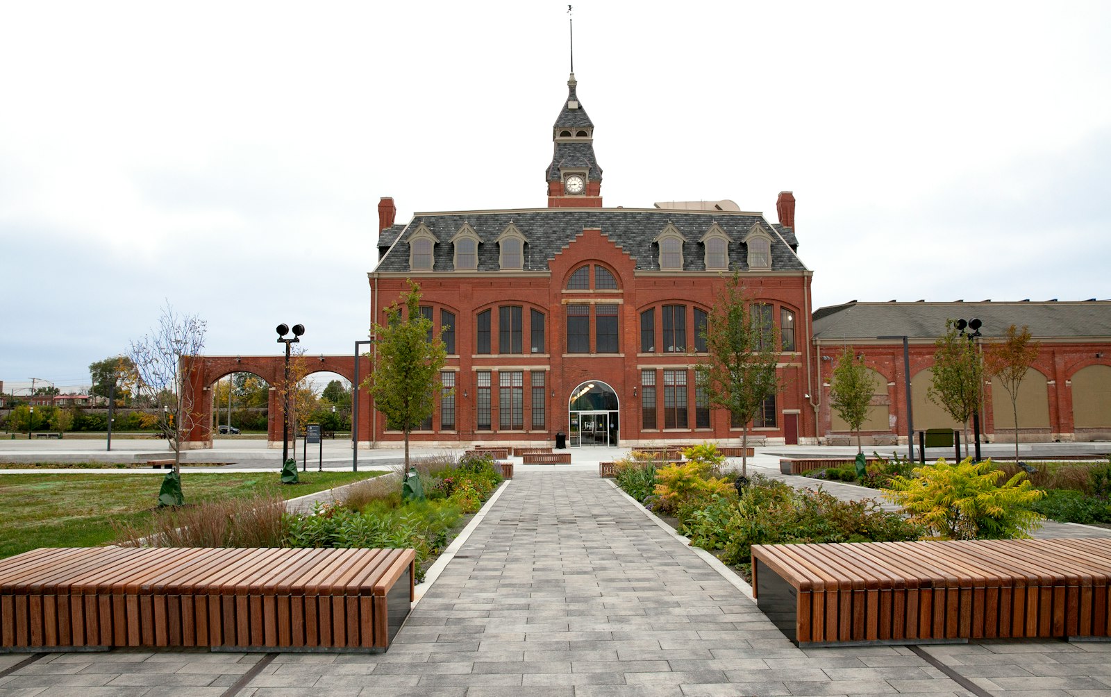 A paved pathway leads up to a three-story red brick building with a clocktower. Around the building are green, manicured lawns and benches