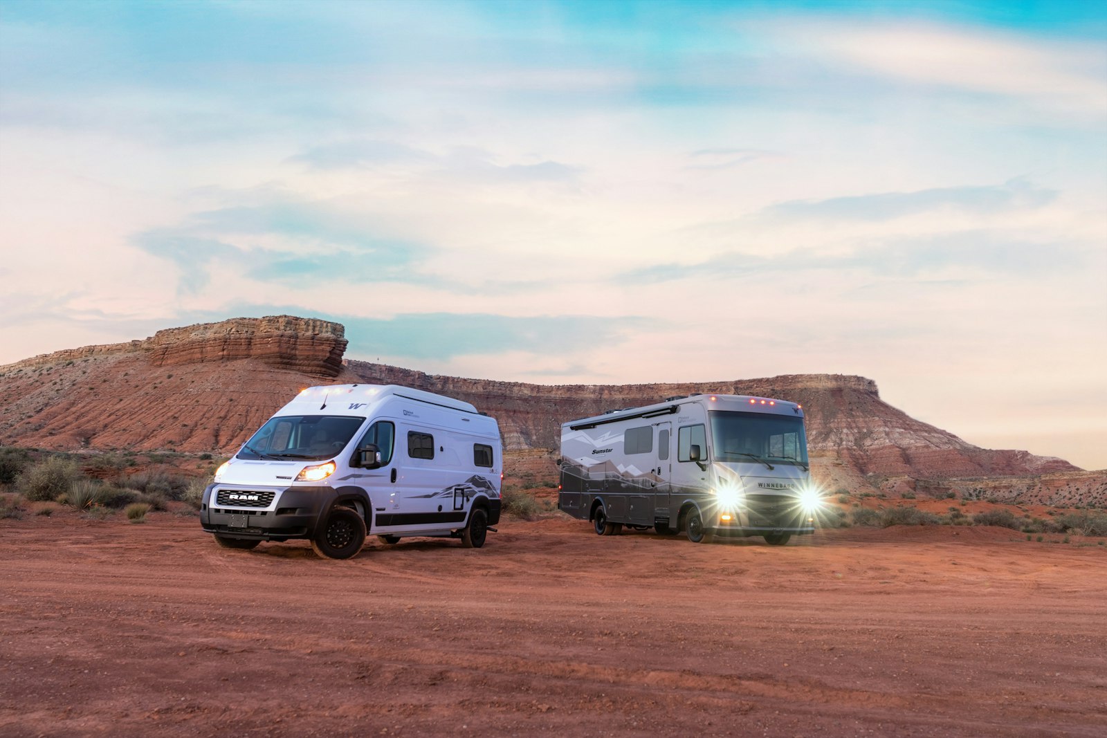 Two RVs are parked, with their lights on, in a desert landscape.