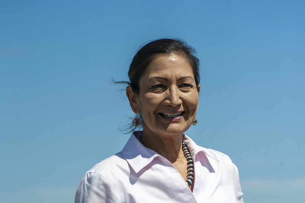 Woman wearing pale pink blouse smiles wide with blue sky and vast ocean behind her.