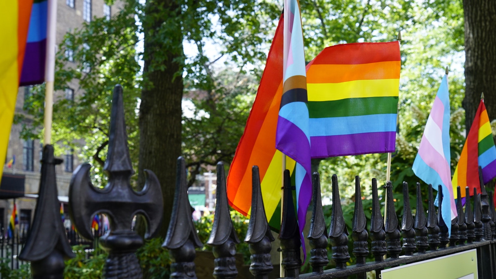Rainbow and LGBTQ+ pride flags along the top of an iron fence surrounding Christopher Park