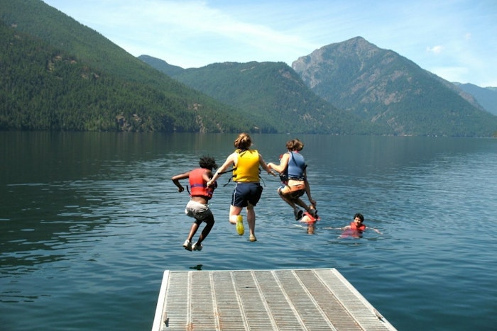 Three kids jump off a dock and into a lake