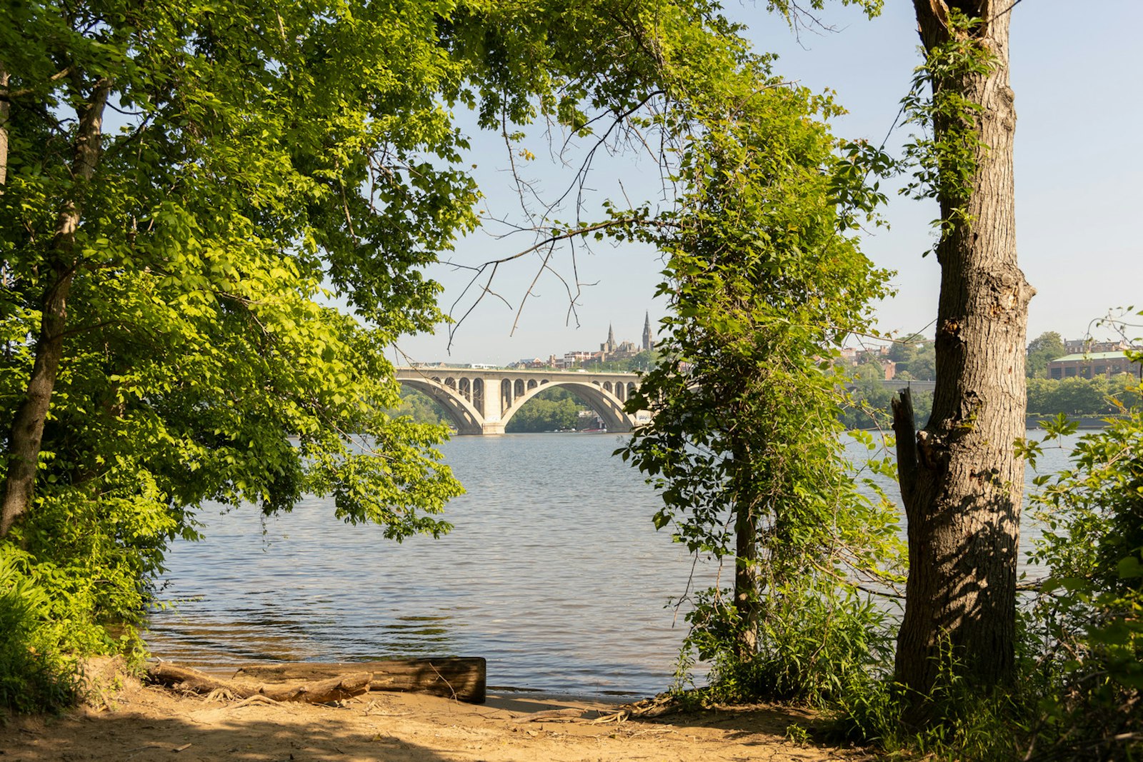 A sandy embankment at the base of a river with the Key bridge in the distance.