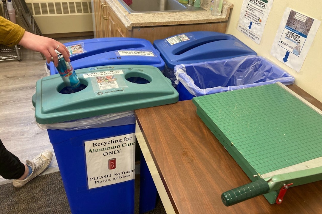 A person drops a can into color-coded recycling bins