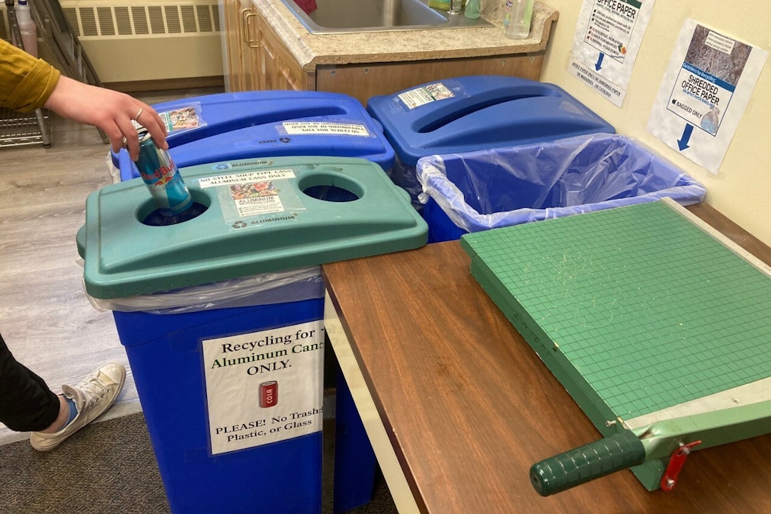 A person drops a can into color-coded recycling bins