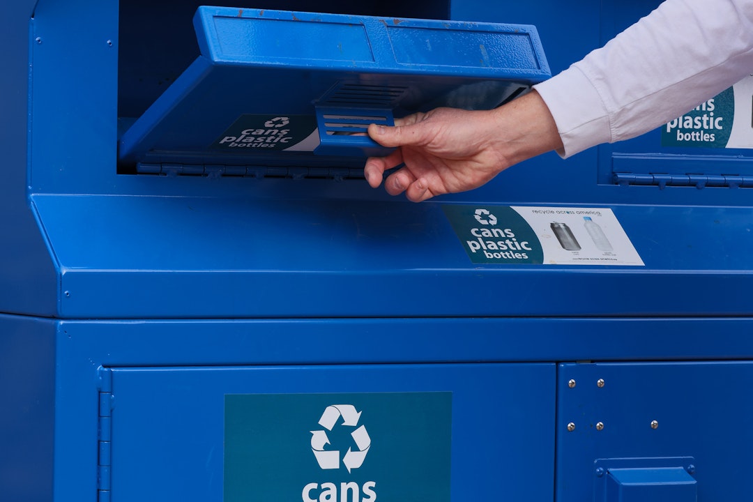 A person drops a plastic water bottle into a blue recycling bin