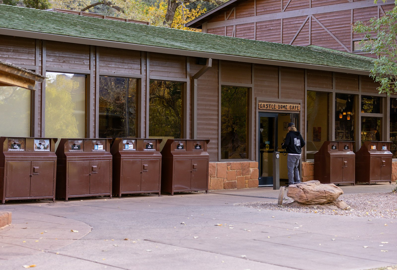 A person walks into a building, the facade of which is lined with brown recycling bins