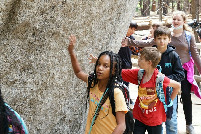 Fourth graders run their hands along a stone wall
