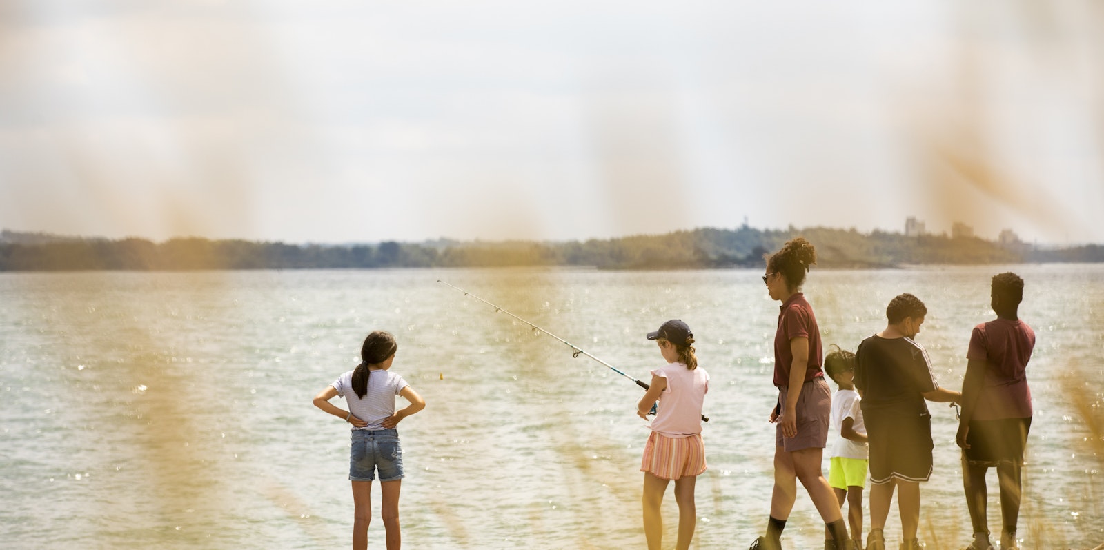 A group of children fly fishing in front of a body of water