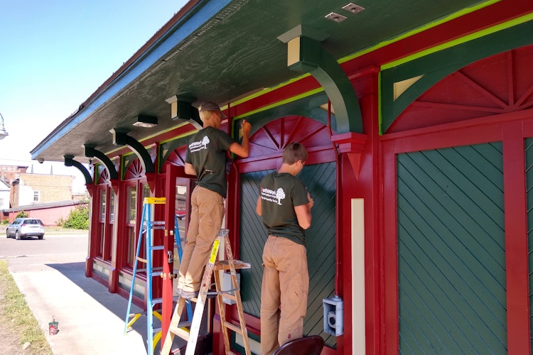 A group of people paint a one-story building with vibrant red and dark green paint