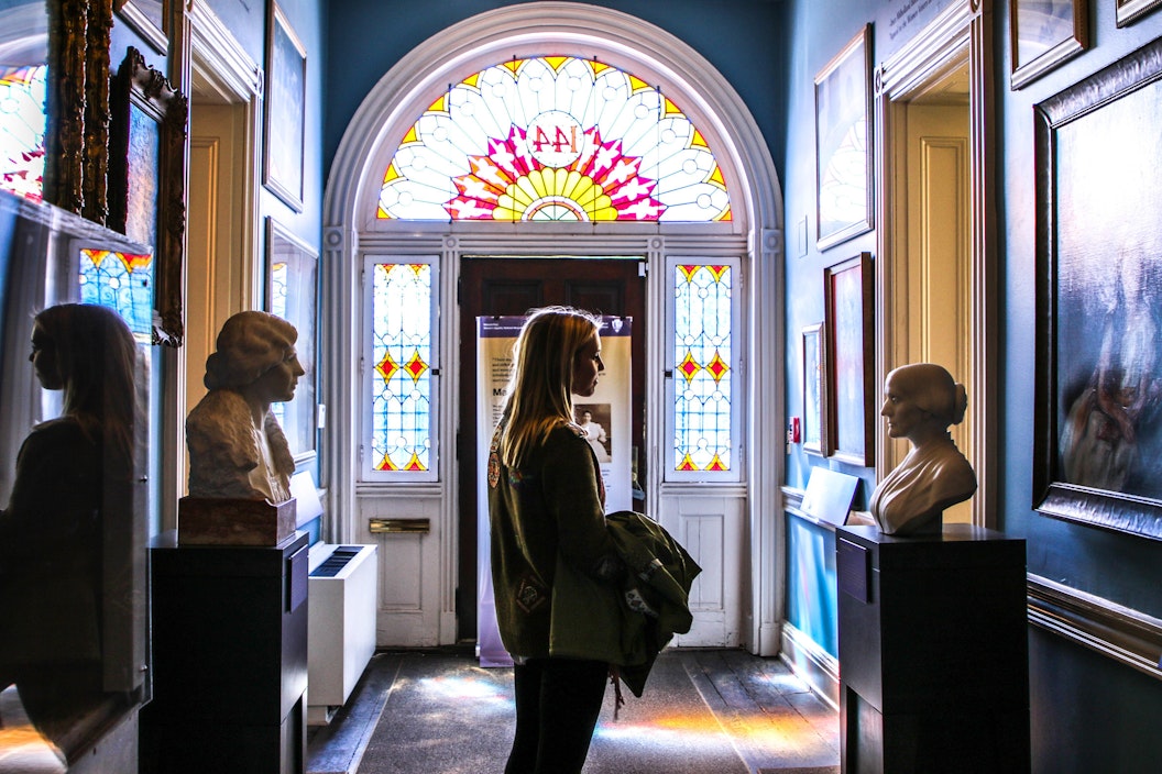 Visitor in a hallway with numerous paintings and busts of suffragists