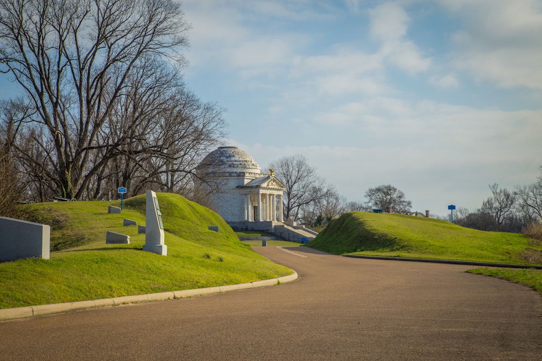 A paved road leads to a classical style stone monument with a domed roof
