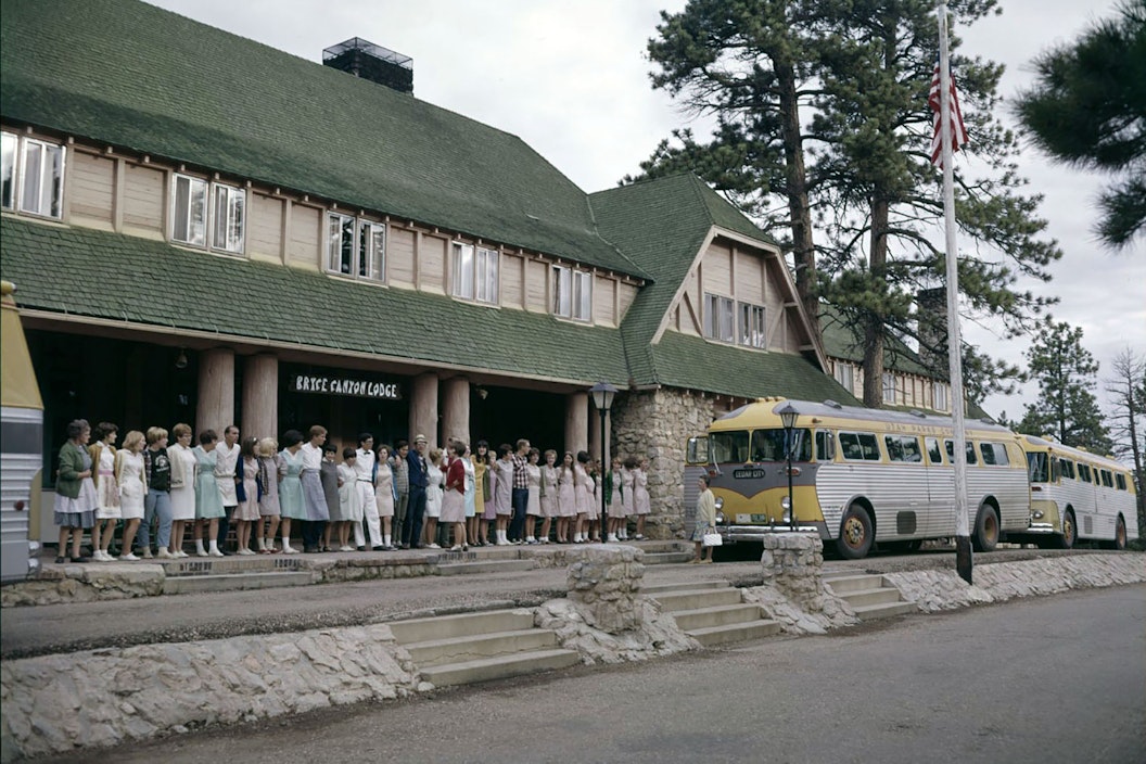 Vintage photo of a group of people standing out front of a lodge and look at a departing bus