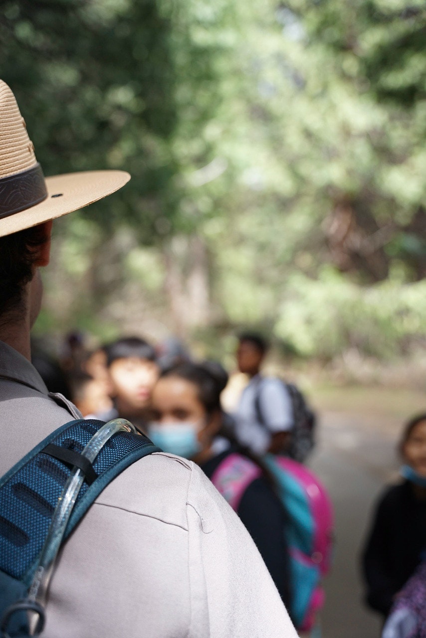 Close up over a ranger (wearing a uniform)'s shoulder as they speak to a group of kids