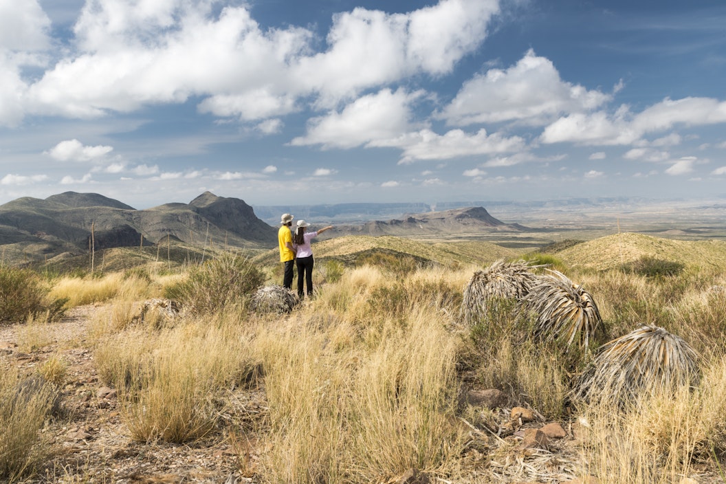 Two people stand in an arid landscape and point toward the horizon
