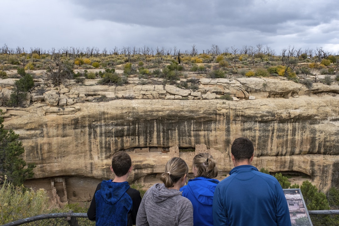 A group of people stand on an overlook point out onto historic Mesa Verde