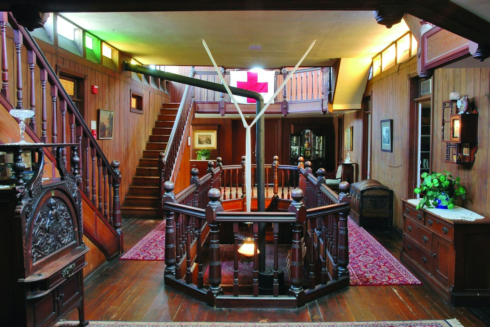 Interior of a wood paneled home with a staircase and a Red Cross flag hanging on bannisters
