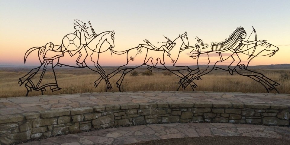 At sunset, a metal sculpture depicts spirit warriors on horses