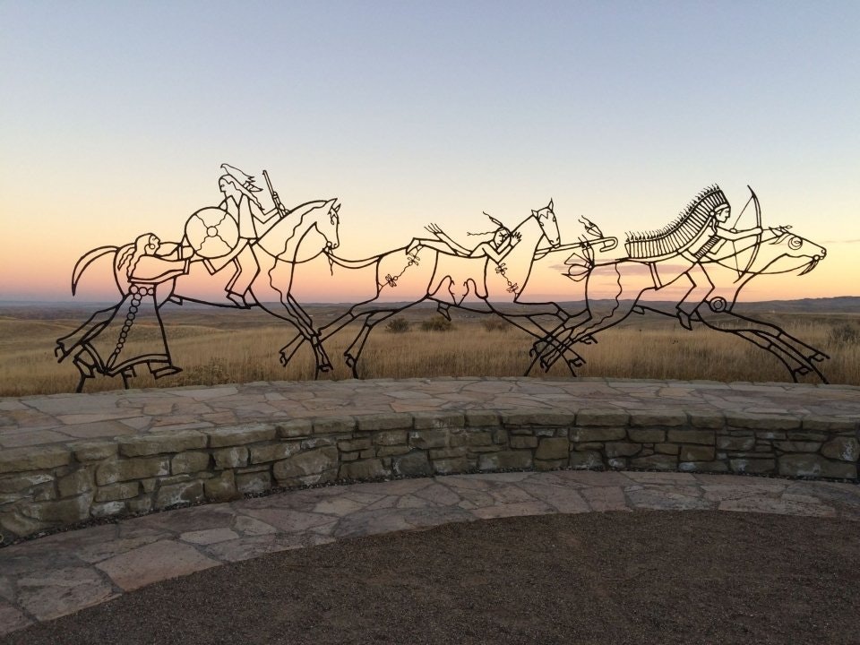 At sunset, a metal sculpture depicts spirit warriors on horses