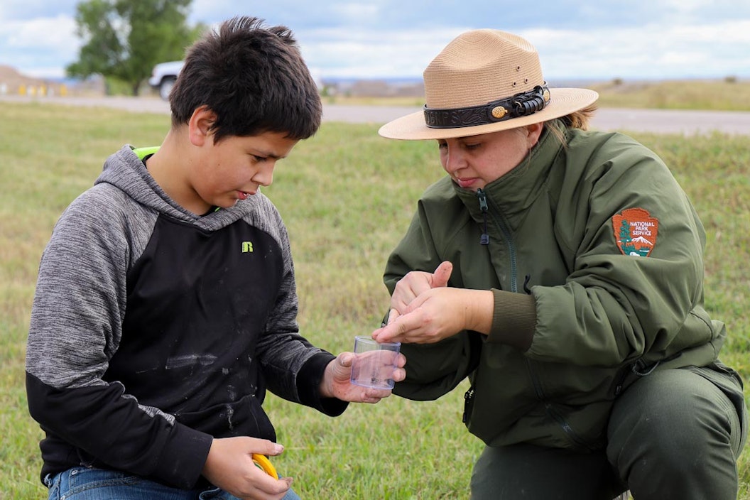 A student and a ranger crouch down to examine a sample, held in a plastic container