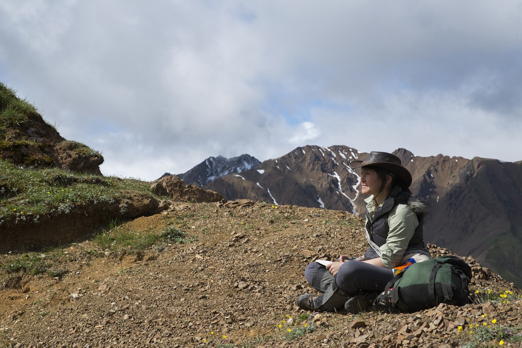 A person sits on a mountain overlook and reflects, gazing into the distance