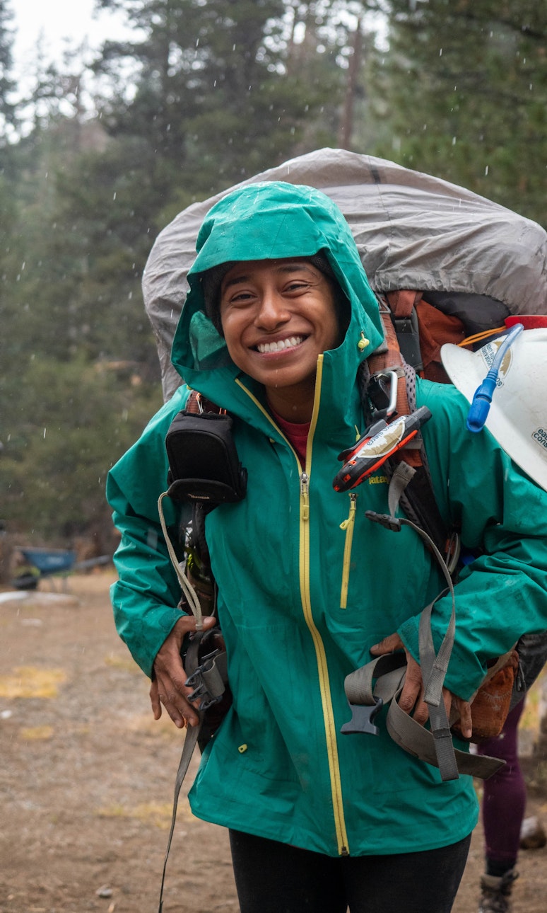 Person decked out in hiking and camping gear smiles at the camera