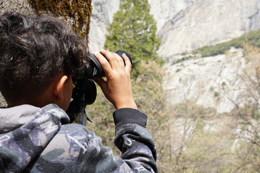 A student uses a pair of binoculars to look at a waterfall in the distance