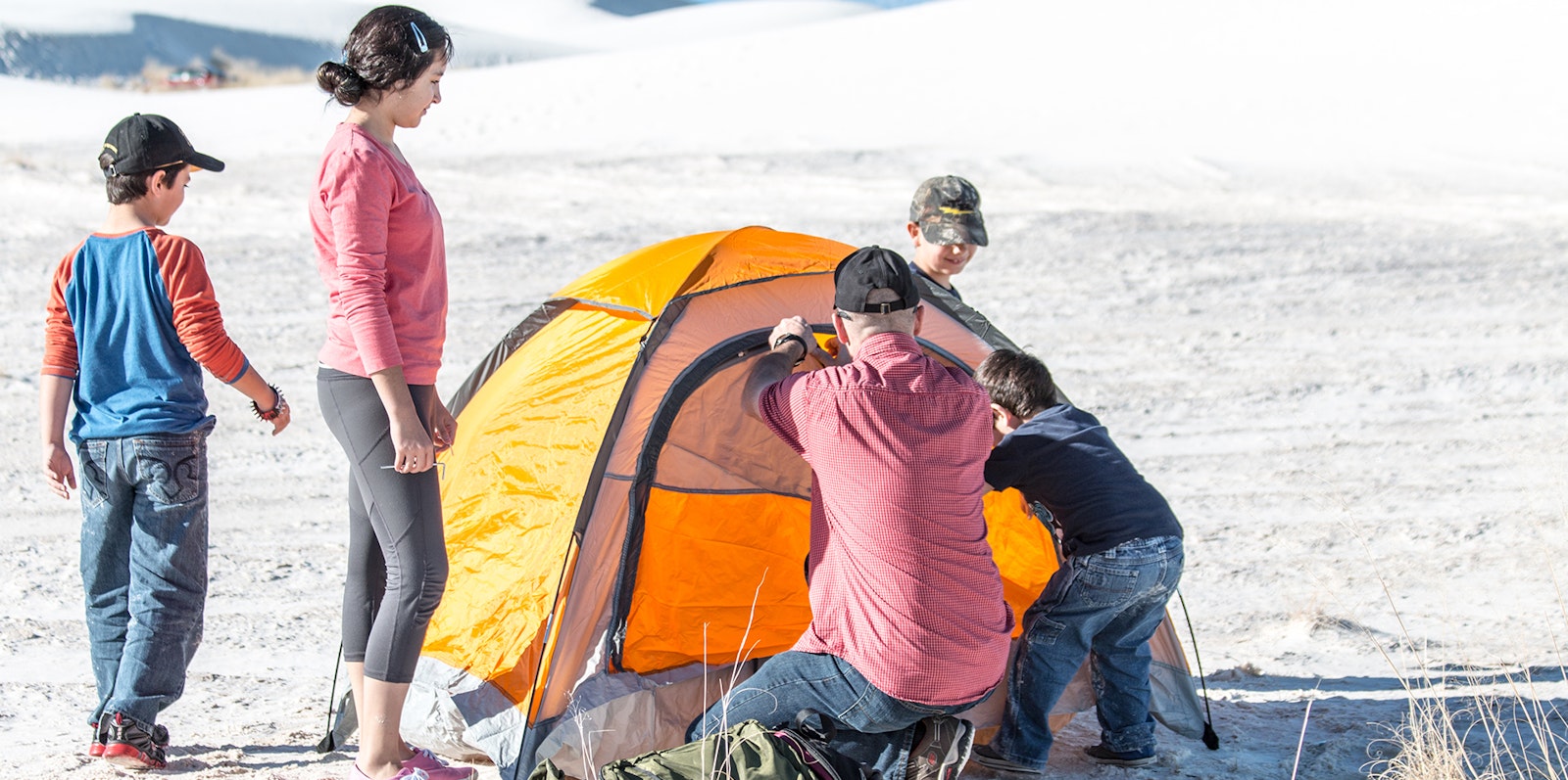 A family sets up a small yellow tent on sand dunes