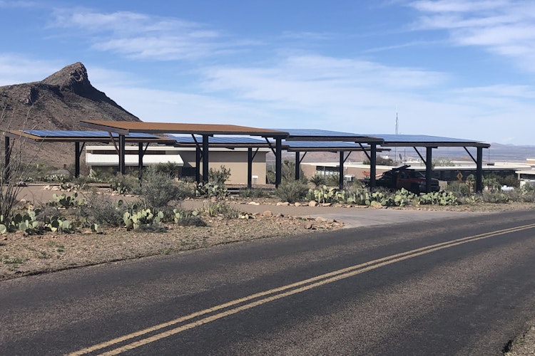 Elevated solar panels sit 10 feet off the ground along a paved road in the middle of a desert