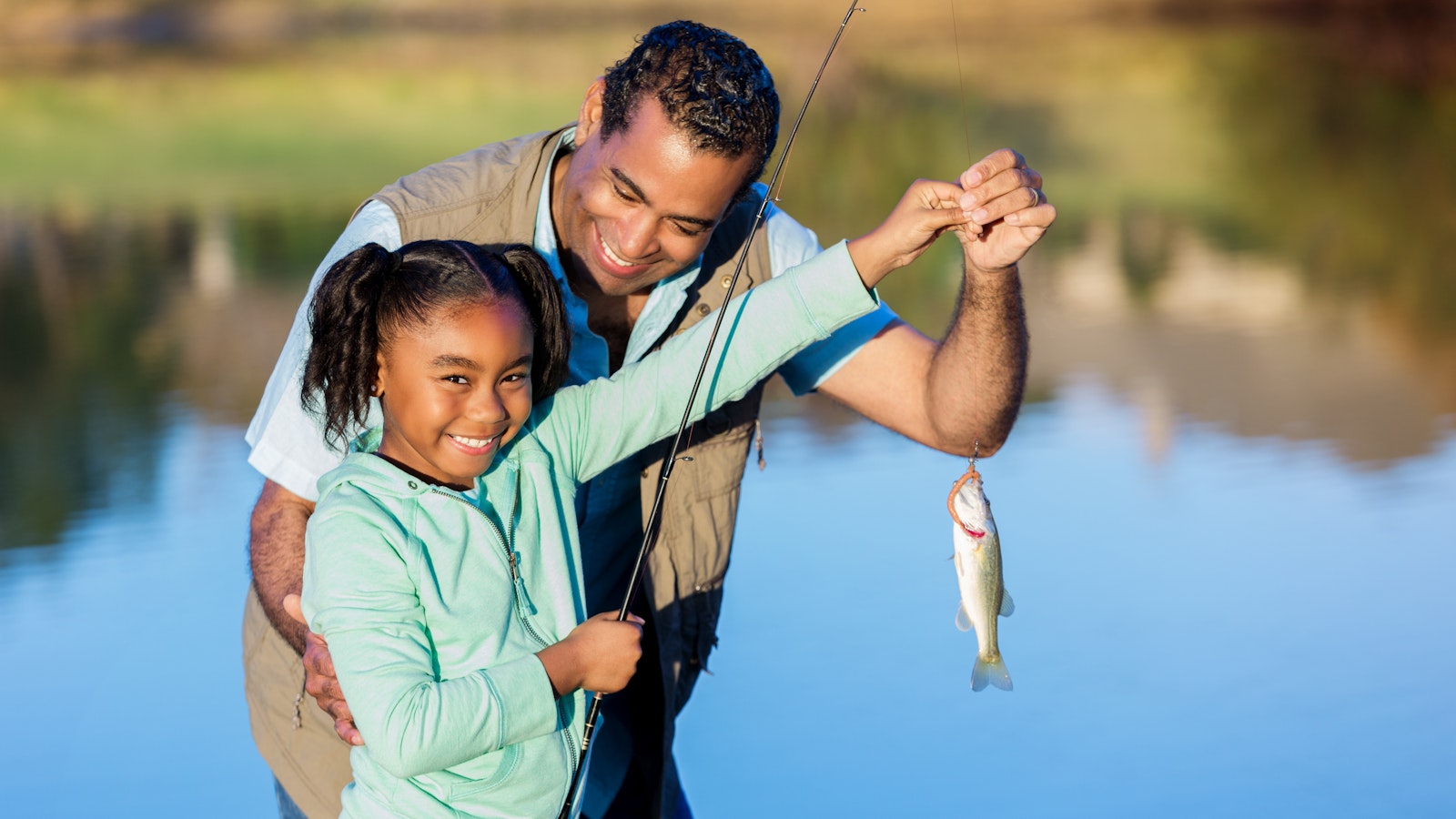 A kid and a parent smile as they hold up a fish on a line